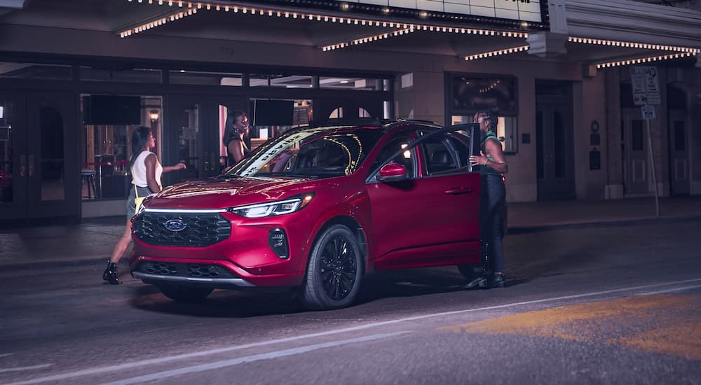 A group of friends getting into a red 2023 Ford Escape parked under a marquee at night.