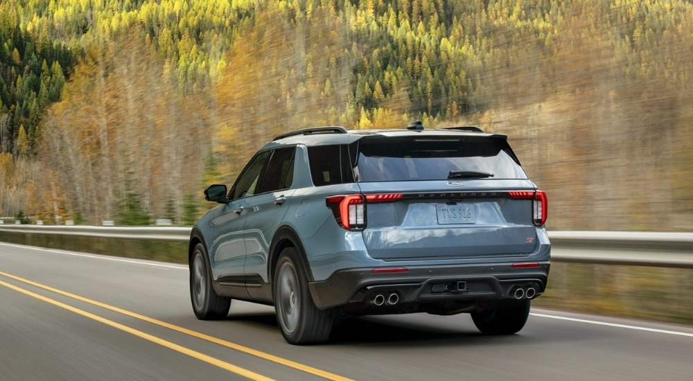 A blue 2025 Ford Explorer ST driving on a tree-lined road.