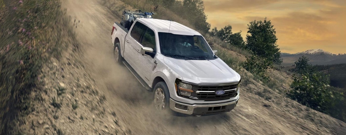 White 2026 Ford F-150 XLT driving off-road down a hill.