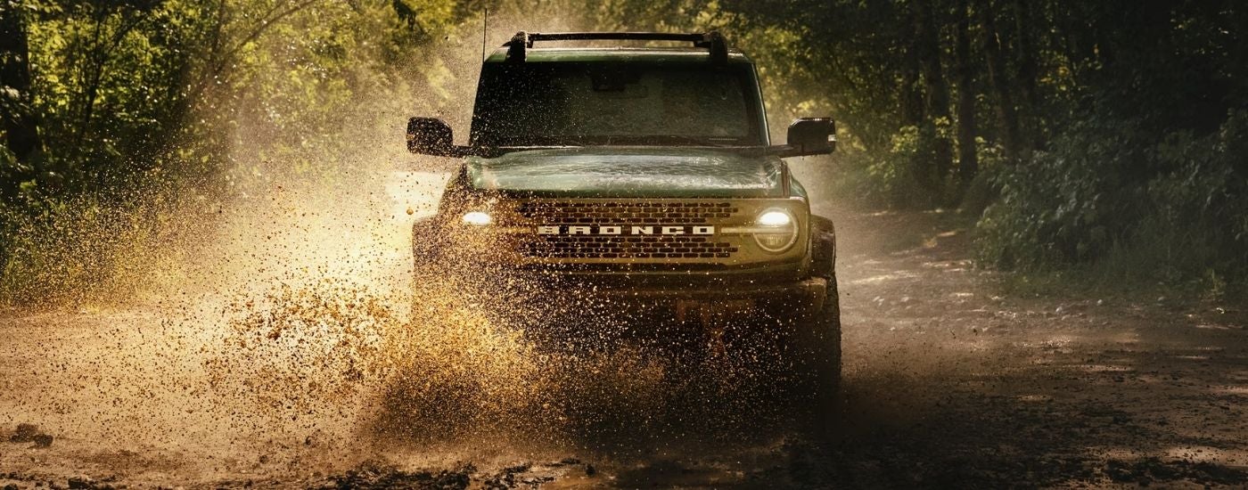 A green 2025 Ford Bronco is shown driving to a Ford dealer.